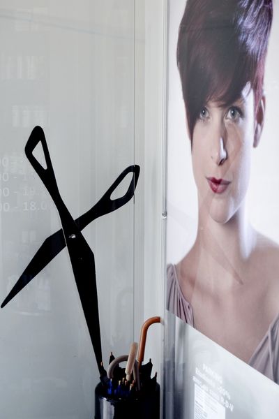 Grands ciseaux décoratifs et affiche de coiffure près de l’entrée