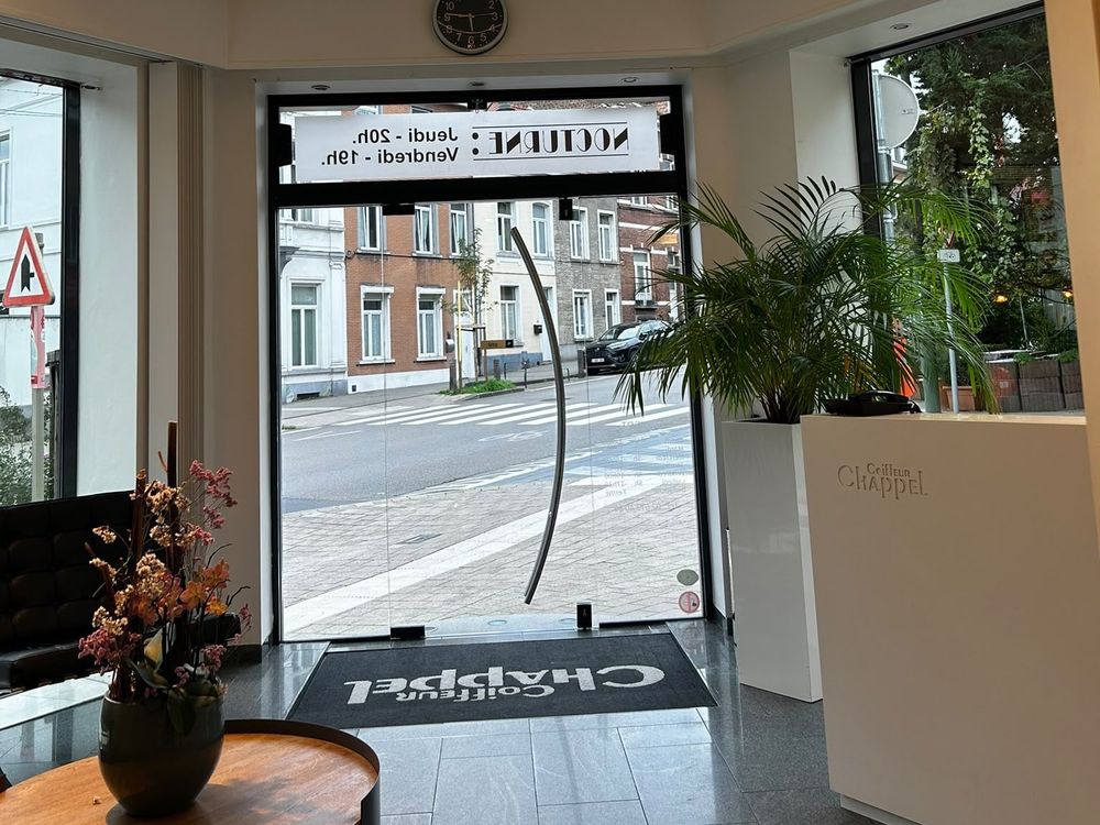 Entrée du salon Coiffure Chappel d’Auderghem, son logo sur le tapis et la rue en enfilade